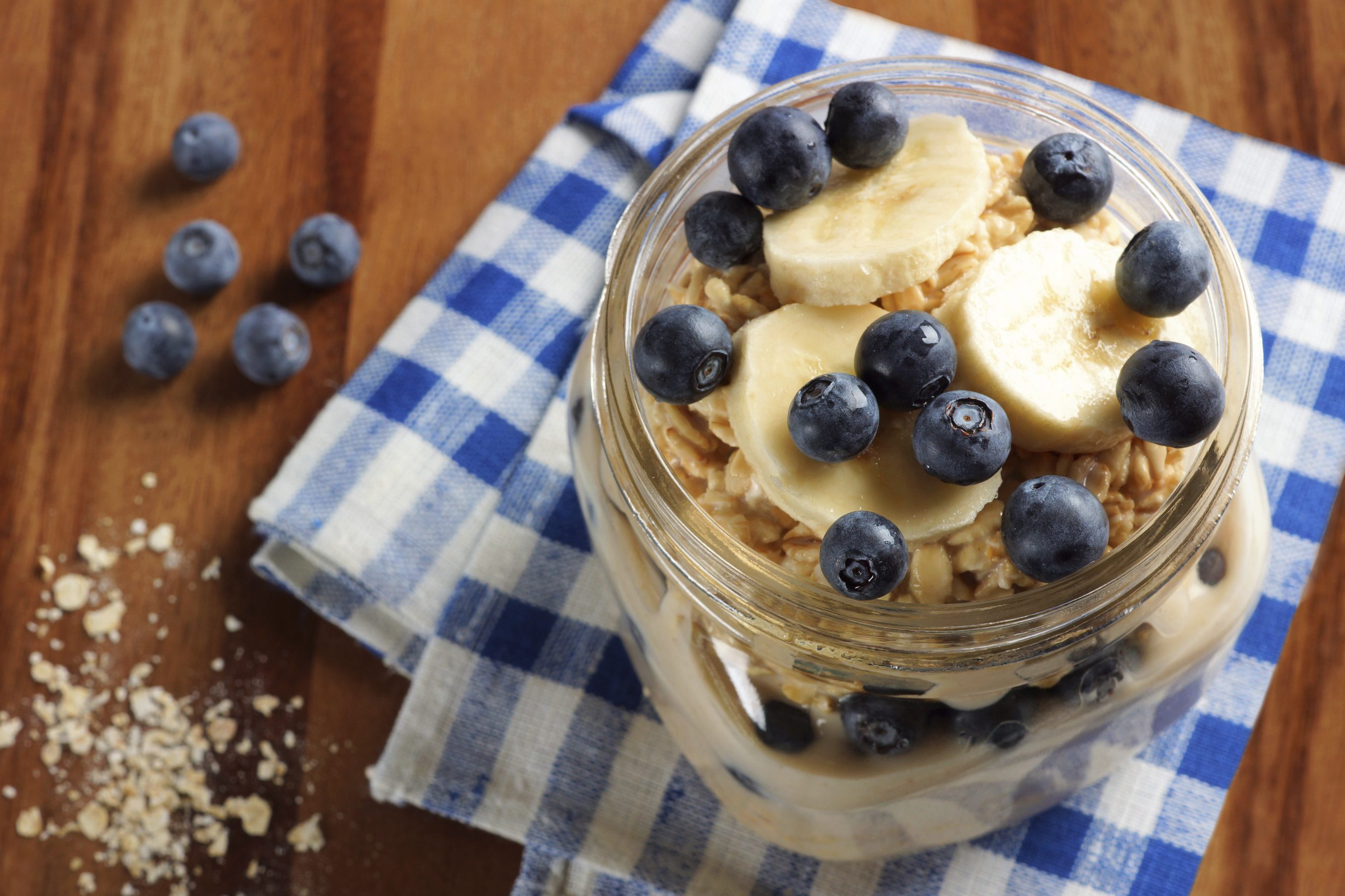 Blueberry and banana breakfast overnight oatmeal in a mason jar, with checkered cloth on wood